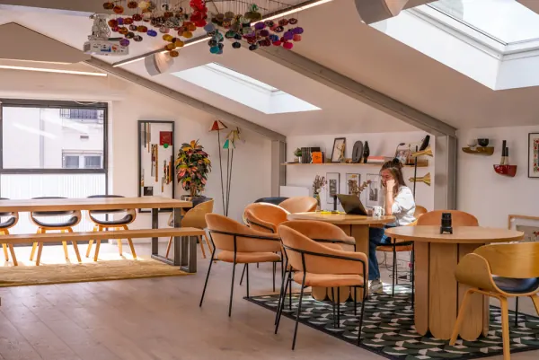 La Grange : salle sous charpente éclairée par des puits de lumière, avec tables rondes et grande table commune