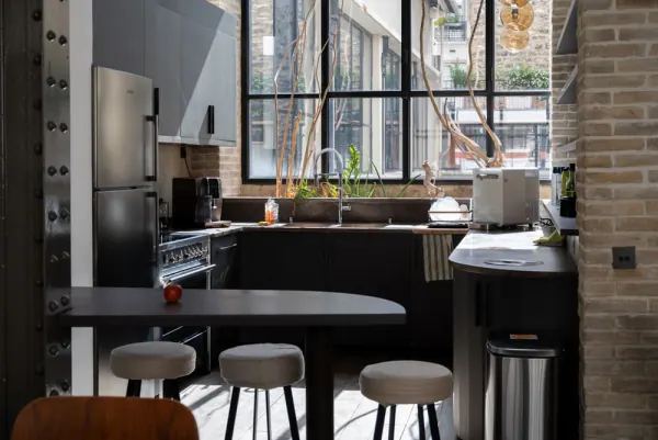 Cuisine équipée du Loft, avec comptoir et tabourets, devant une verrière industrielle